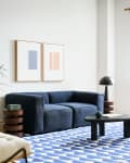 Living room with blue sofa, white walls, art over sofa, natural color armchair, Marimekko/West Elm collab blue and white patterned rug