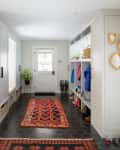 White entry way with dark tile floors and red vintage runners, built in cubbies for boots and coats
