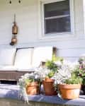 Golden bells create a farmhouse vibe on a front porch with seating and potted plants.