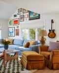Living room with sectional sofa, arm chair with ottoman, accent chairs, coffee table, checkered area rug, potted plant, lamp, gallery wall, and guitar on wall.