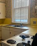 A small kitchen with white cabinets, yellow countertops, a double sink, and a stove with blue decorations.