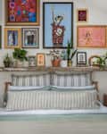 Colorful gallery wall above a bed with striped pillows, wooden nightstands, and various plants.