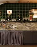 A stylish bar area featuring a green tiled wall, marble countertop, and glassware.
