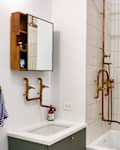 Bathroom with copper pipe shower, white curtain, green vanity, and wall-mounted mirror cabinet