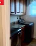 Laundry room with wooden cabinets, a washing machine, and a window with blinds.