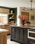 Modern kitchen featuring a large island with a marble countertop, dark cabinetry, and a vase of pink flowers.