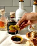 Hand dipping bread in olive oil and vinegar with Brightland bottles in the background.