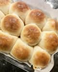 Golden-brown dinner rolls arranged in a glass dish lined with parchment paper.