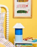 Colorful children's bedroom with a white bed, plush toys, yellow walls, and a blue lamp on a nightstand.
