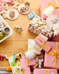 Gifts sit under a christmas tree, while a platter of sweet rolls, fruit, and tea are on the floor ready for Christmas Breakfast.
