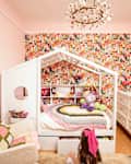A colorful children's bedroom featuring a house-shaped bed, floral wallpaper, plush toys, and a decorative dresser.