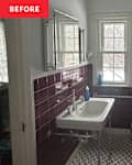 Bathroom with burgundy tiled walls, a white sink on a metal stand, and a window. A towel hangs on the door.