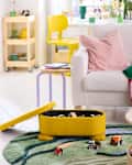 Bright living room with a yellow storage box, colorful toys, a white sofa, and a green rug.