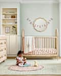 A cozy nursery featuring a wooden crib, a child playing on a round rug, and soft pastel decor.