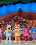 Live performance featuring costumed characters Bluey and Bingo, with performers in colorful outfits on a vibrant stage.