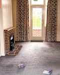 Living room with a brick fireplace, floral curtains, and a gray carpet, featuring scattered children's shoes.