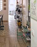 Hallway with patterned tile floor, wooden dining table, green shelving unit, and colorful decor items.