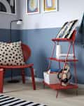 Cozy corner with a red chair and a red shelving unit holding books, headphones, and decor, against a blue wall.