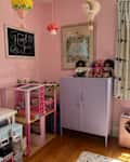 Purple storage cabinet filled with doll accessories, three dolls on top, and a pink salon playset beside it.