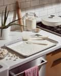 Baking tray with white batter and sprinkles, spatulas, rolling pin, and flour jar on a kitchen counter.
