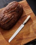 Sourdough loaf and serrated knife on a wooden cutting board.