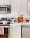 Modern kitchen with stainless steel appliances, floral curtains, a white pot on the stove, and colorful utensils on the counter.