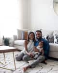 Family sitting on a patterned rug in a living room with a beige sectional sofa, geometric pillows, and a round mirror.