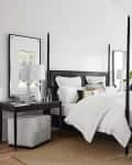 Modern bedroom with a black four-poster bed, white bedding, two gray armchairs, and large windows with outdoor views.