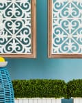 Vase of white hydrangeas and bowl of lemons on blue wicker table, with decorative wall panels and green plants.