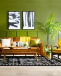 Mid-century modern living room with green walls, yellow chairs, brown sofa, black and white rug, and potted plants.
