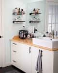 Bathroom with white vanity, square sink, and shelves of toiletries. Frosted glass door and bathtub visible.