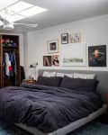 Bedroom with open closet, dark bedding, blue rug, and wall art. White dresser with decor items on the left.