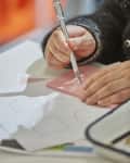 Person using a craft knife to cut shapes on a pink cutting mat.