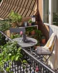 Small balcony with a round table, two chairs, potted plants, and a cozy blanket.