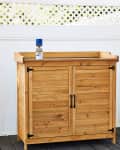 Wooden outdoor cabinet with black handles on a deck, white lattice fence behind, and a can of spray paint on top.