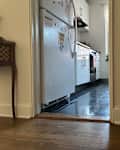 View of a kitchen with white cabinets and a refrigerator, featuring a night light on the wall near the doorway.