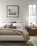 Cozy bedroom featuring a bed with neutral bedding, decorative pillows, a wooden nightstand, and a lamp by the window.