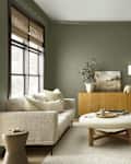 Cozy living room with olive green walls, a light sofa, round coffee table, wooden sideboard, and decorative items.