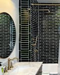 Modern bathroom featuring dark green tile, a white shower curtain with storage pockets, and a round mirror.