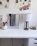 White desk with jewelry organizer, makeup brushes, mirror, lamp, and photo display on the wall.