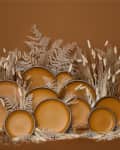 Stacked brown ceramic plates surrounded by dried grasses and ferns.