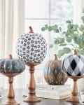 Decorative pumpkins with geometric patterns on wooden stands, surrounded by candles and books.