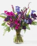 Vibrant bouquet with purple, pink, and blue flowers in a clear glass vase.