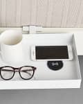 White tray with a mug, eyeglasses, and a smartphone on a wireless charging pad.