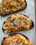 Three slices of toasted bread topped with cheesy cauliflower, chives, and grated cheese on parchment paper.