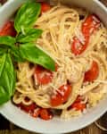 bowl of spaghetti with cherry tomatoes and basil leaves on a wooden table