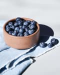 Bowl of fresh blueberries on a light blue cloth, casting shadows.