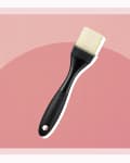 Black-handled pastry brush with white bristles on a pink geometric background.