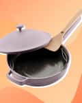 Purple non-stick frying pan with lid and wooden spatula on an orange abstract background.