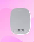 Digital kitchen scale with a gray surface and LCD display on a pink abstract background.